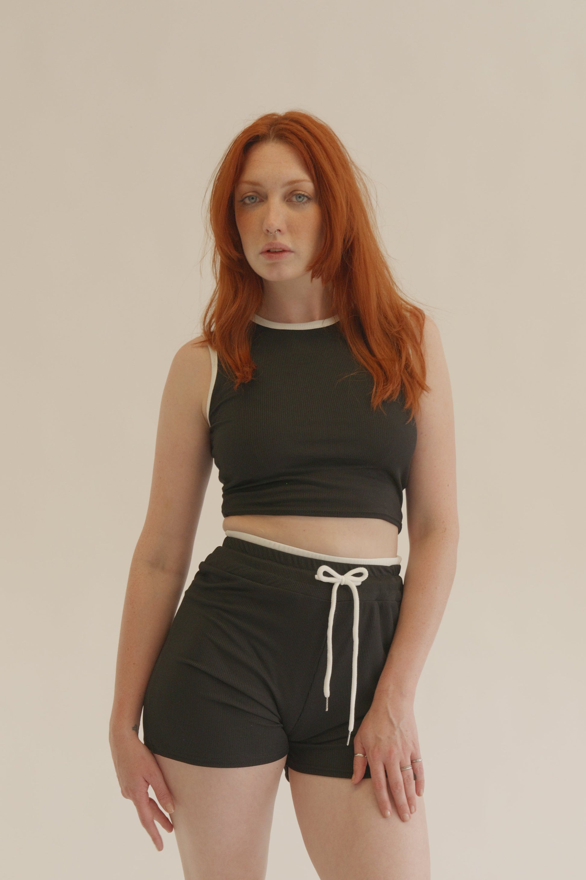 Person wearing a black tank top and shorts on a beige background